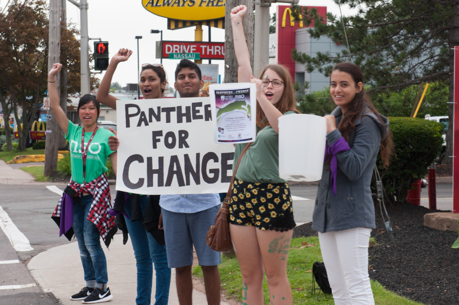 Cheering students stand at a street corner. They hold a sign reading "Panthers for Change."