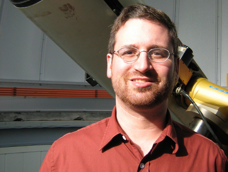 A smiling man in front of a telescope
