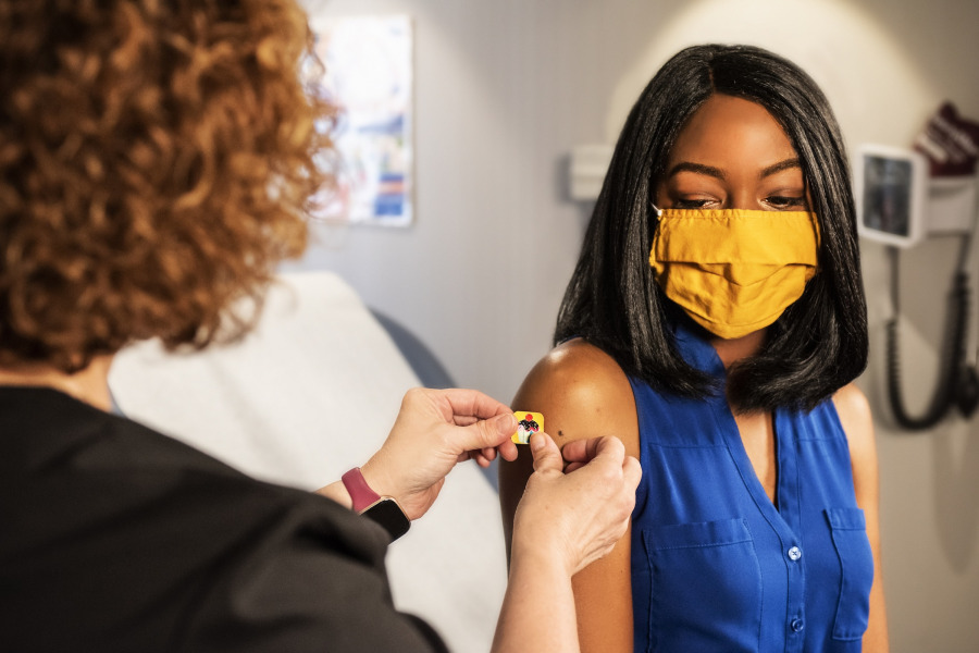 photo of woman applying a plastic bandage to another woman's after receiving a vaccination