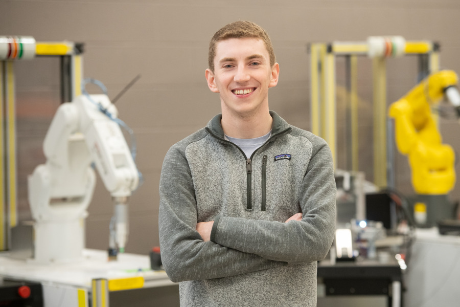 photo of young man standing with arms folded in front of engineering lab equipment