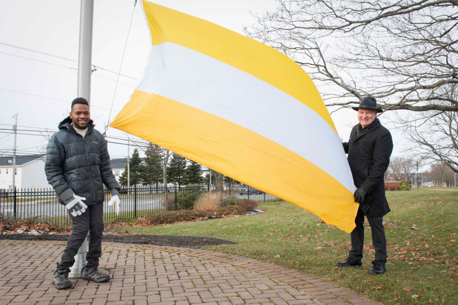 photo of two men standing near a flag pole; one holding the corner of the disability flag