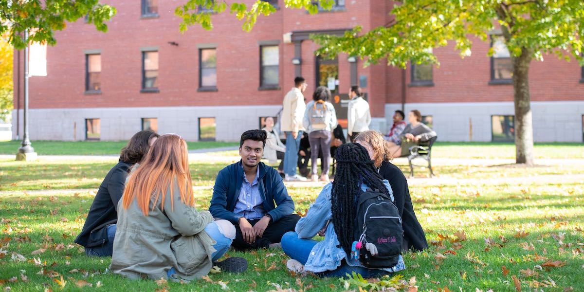a group of five students sitting in the UPEI quadrangle in fall