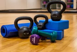 Exercise equipment sits on the ground, including free weights, kettle bells, and a yoga mat
