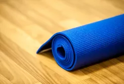 A yoga mat sits rolled up on the ground on the wooden floor of an exercise studio