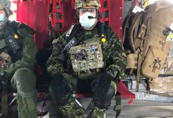 A man in a military uniform strapped with medical gear and a helmet