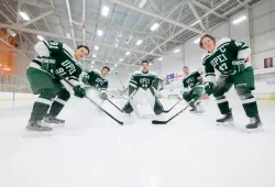 Five members of the UPEI men's hockey team in full gear pose on the ice of the MacLauchlan Arena