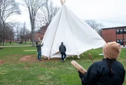 photo of people installing tipi with woman in foreground with drum