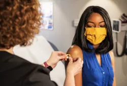 photo of woman applying a plastic bandage to another woman's after receiving a vaccination