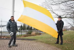 photo of two men standing near a flag pole; one holding the corner of the disability flag