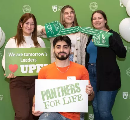 four UPEI students in front of a green backdrop with white and green balloons 