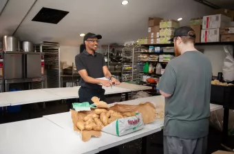 a smiling man speaking with another man peeling potatoes