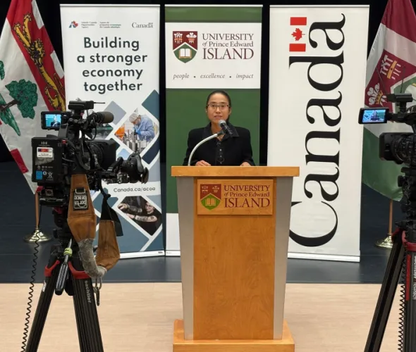 Dr. Beibei Jia, Assistant Professor, Epidemiology, AVC, speaks at the news conference announcing funding for shellfish health research and resilience projects. Photo of a woman standing at a podium flanked by video cameras