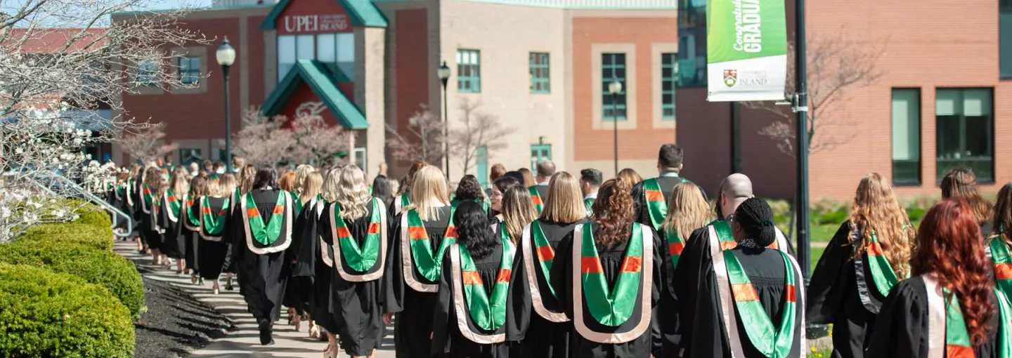 a procession of UPEI graduates wearing gowns and hoods 