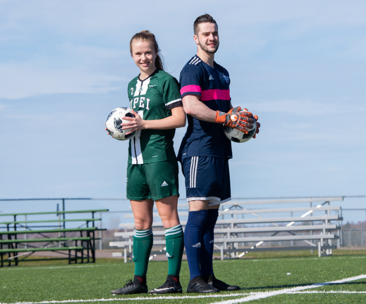 A female and a male soccer player stand back to back