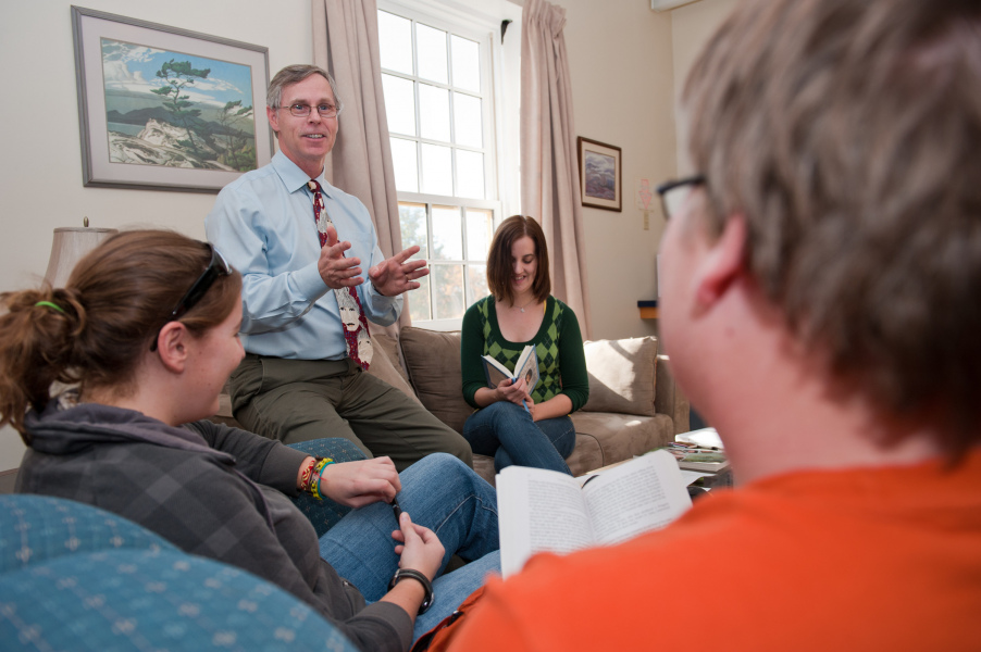 A male teacher in a tie speaks in an animated way with a group of students