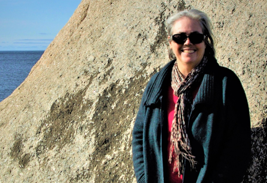 Dr. Terry Whitebeach A smiling woman standing on a rocky beach