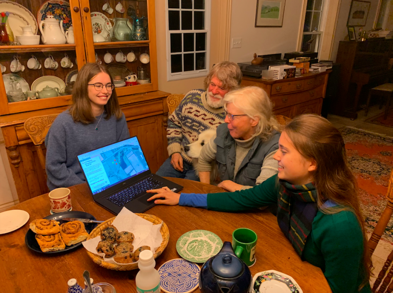 Two female students and a male and female farmer sit around a farmhouse table