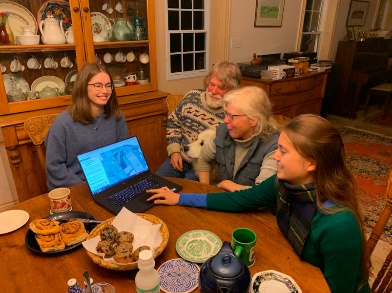 Two female students sit around a farm table speaking with an older couple