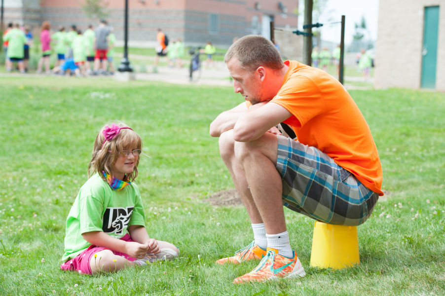 A young girl sits on the grass speaking with an adult