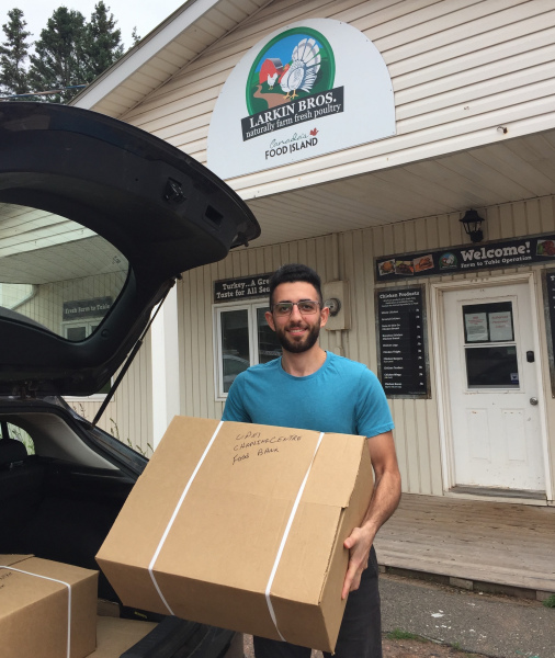 A smiling male student loads a large box into the back of a vehicle