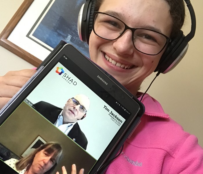 A 2020 SHAD participant during the keynote address of Dr. Donna Strickland A young female holds up a digital tablet with the faces of a man and a woman on it