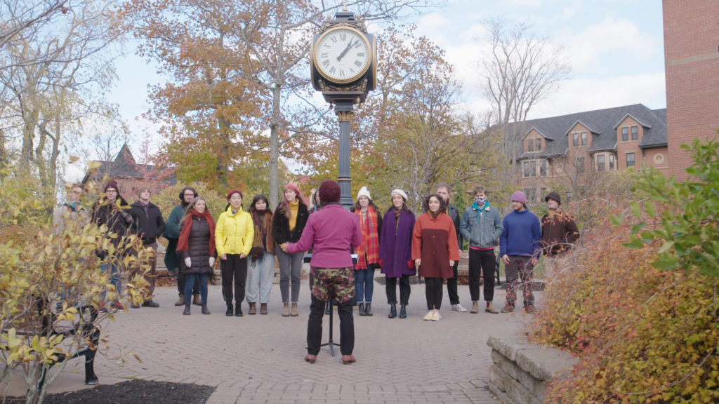 A group of male and female students are singing outdoors on campus