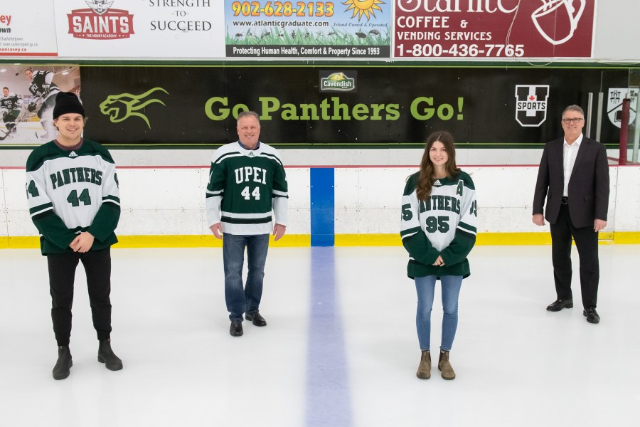 Matt Brassard, David Currie Jr., Faith Steeves, Doug Currie Four people stand on a skating rink surface. A young male hockey player, an older man, a young female hockey player, and another older man
