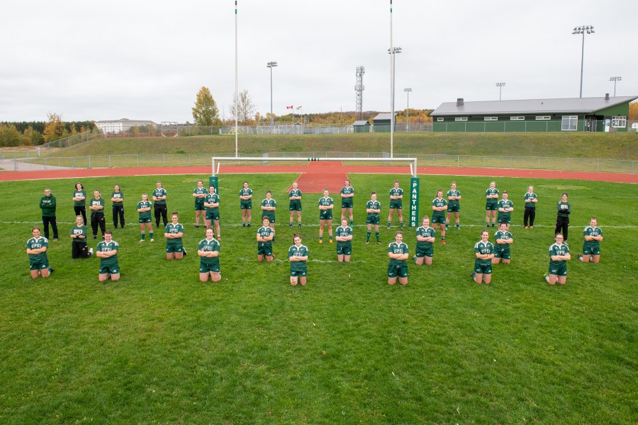 A group of female ruby players stand on a grass sports field