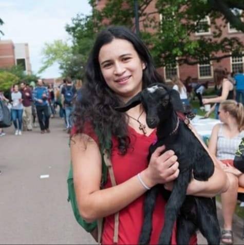 A female student on on a busy campus holding a baby goat