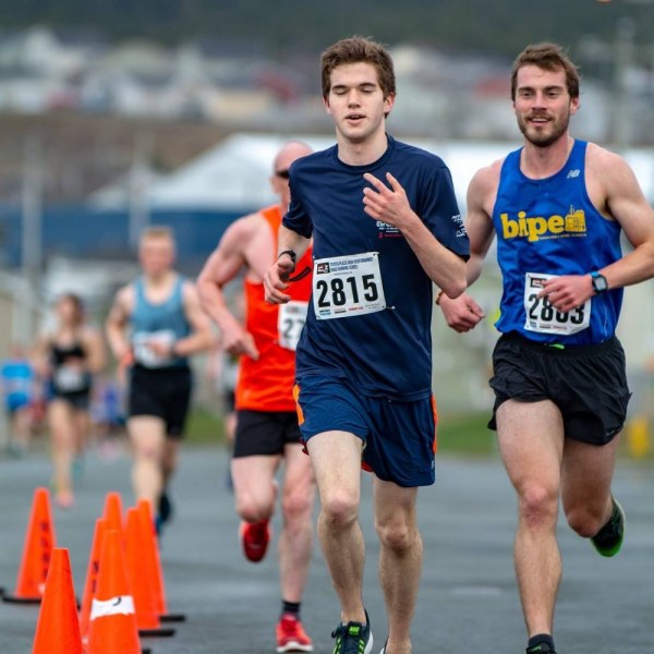 A young man running in a road race looking strong and confident with other runners trailing him