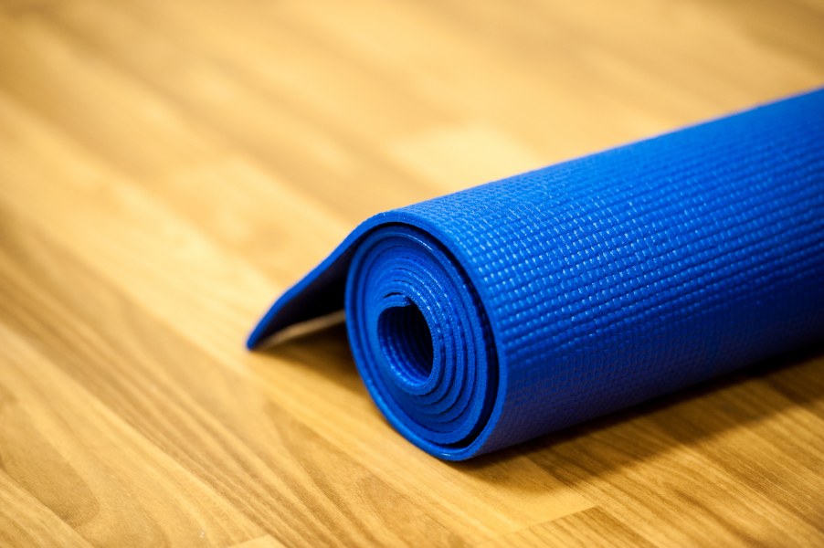 A yoga mat sits rolled up on the ground on the wooden floor of an exercise studio