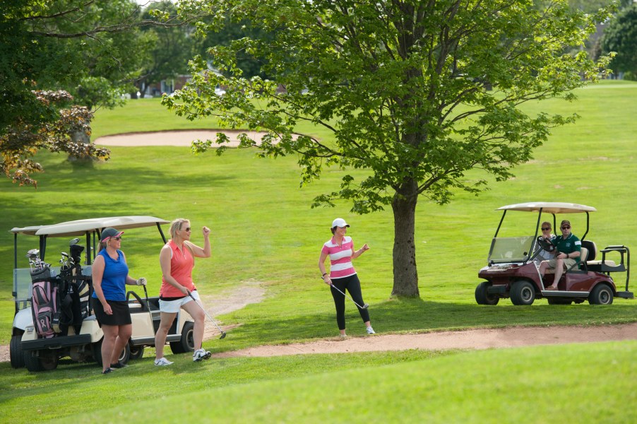 A scene on a golf course from a previous Panther Golf Classic. A pair of female golfers celebrate a shot, out of frame, with their arms in the air.