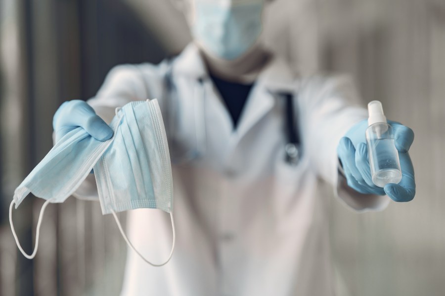 Image of person in lab coat wearing a mask and holding masks and sanitizer