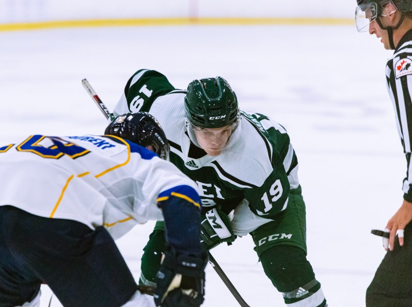 A male hockey player in green and white Panthers gear prepares to take a face-off against an opposing player