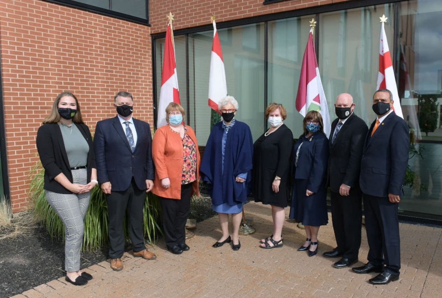 A group photo of men and women standing in front of an array of flags from PEI and Canada