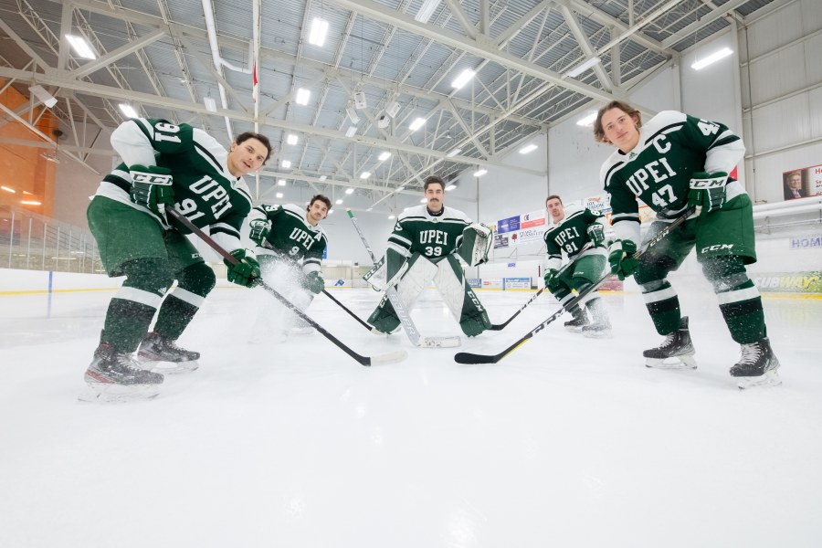 Five members of the UPEI men's hockey team in full gear pose on the ice of the MacLauchlan Arena