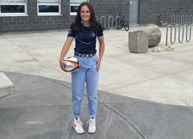 Lauren Bull A female athlete wearing jeans and a T-shirt, holding a rugby ball in a casual setting in front of her high school
