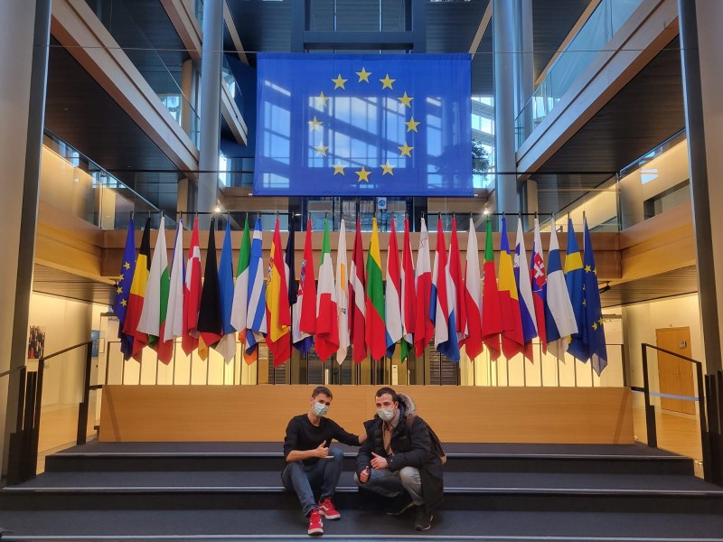 Image of two men sitting on steps in front of a group of flags