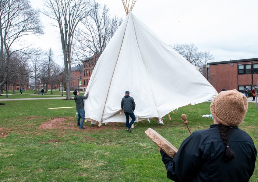 photo of people installing tipi with woman in foreground with drum