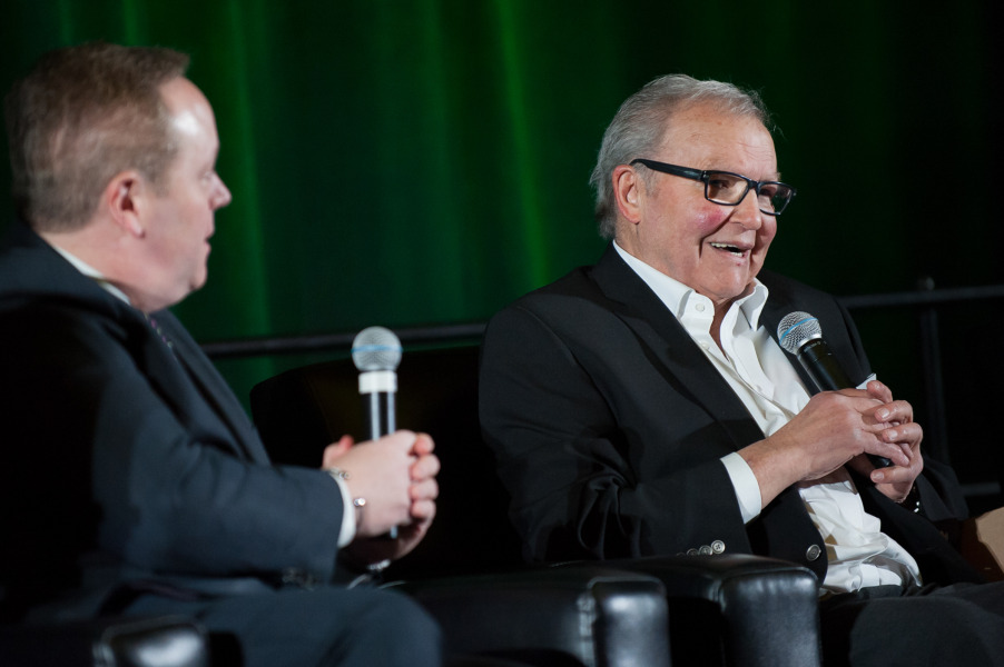 The great Billy MacMillan tells a story to MC Bruce Rainnie and the audience at the 2017 UPEI Sports Hall of Fame induction ceremony. Two men sitting on a stage holding microphones