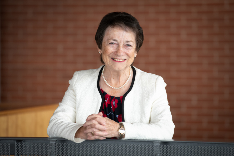 Photo of a smiling woman with hands folded leaning on a railing