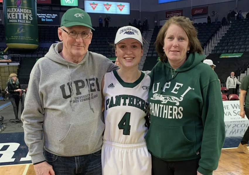 Tracy Ellsworth, far right, pictured with her husband Paul and daughter Jenna Mae, after UPEI Women's Basketball won the 2020 AUS Championship in Halifax photo of man and woman standing on either side of basketball player, all wearing UPEI branded clothing