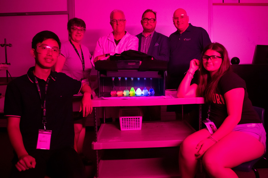 Kevin Jiang (seated left) and Nicola Alexiou (seated right) were among the SHAD students who learned about fluorescence from Dr. Brian Wagner, professor of chemistry (second left, back row). Looking on are Dr. Charlene Van Leeuwen, SHAD UPEI program coordinator; Paul Ledwell (second right, back row), SHAD board member and UPEI’s Deputy Minister University Champion; and Tim Jackson, President and CEO of SHAD. The group is gathered around a UV-A lightbox that contains seven fluorescent solutions showing the colours of the rainbow. SHAD participants