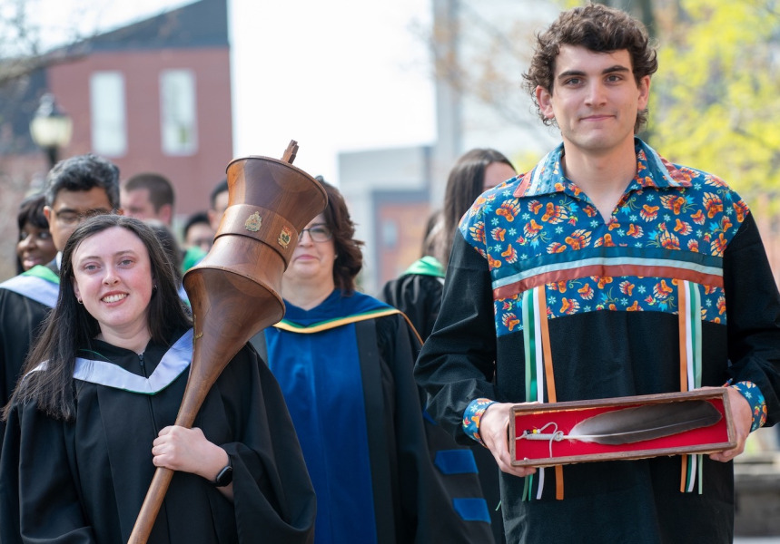 Photo of person carrying ceremonial mace and person carrying Eagle Feather leading a procession