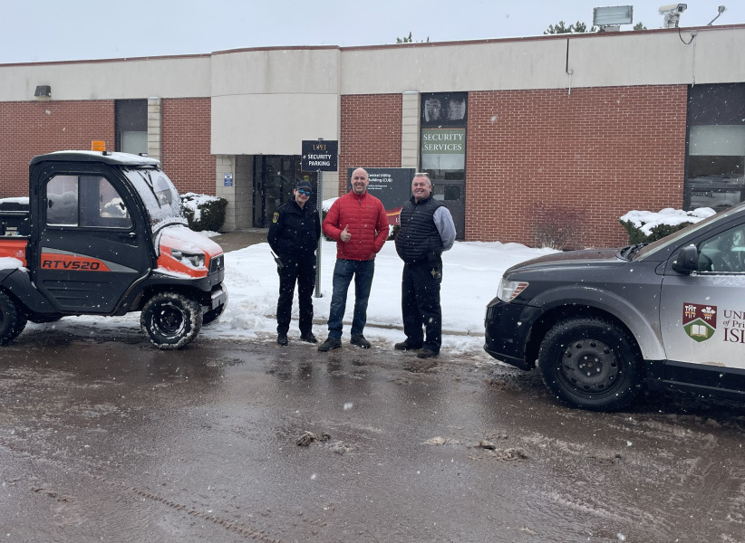 photo of three people standing between two vehicles in front of a brick building