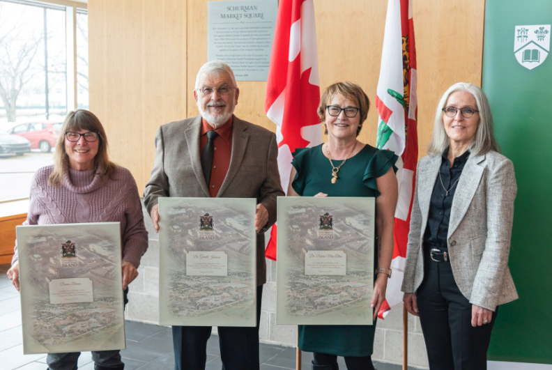 Photo of four people standing in a group, three of them holding canvas recognition frames