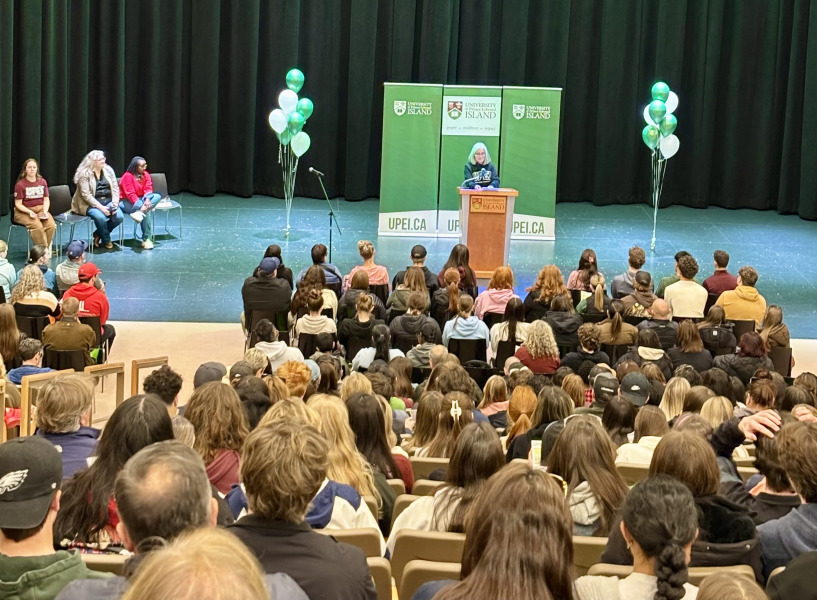 Photo of woman speaking at a podium on stage before a large audience