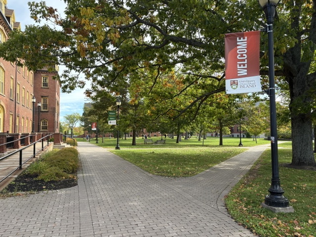 Photo of welcome banner on lampstand in campus quadrangle along a brick walkway