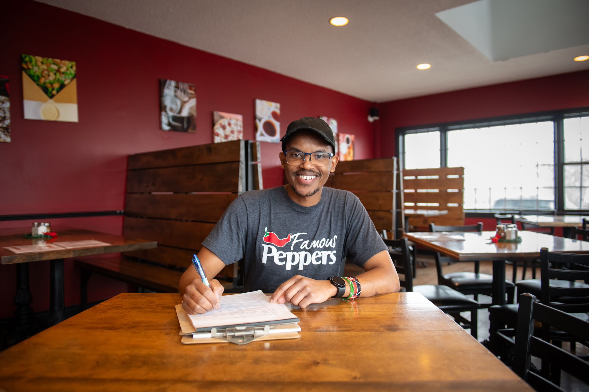 a smiling man sitting at a restaurant table writing on a clipboard