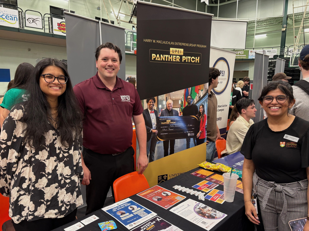 Two people standing behind a table with brochures on it speaking to a woman